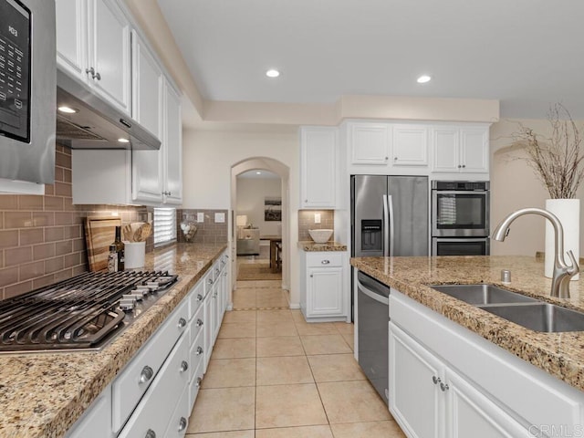 kitchen featuring arched walkways, light tile patterned floors, appliances with stainless steel finishes, white cabinetry, and a sink