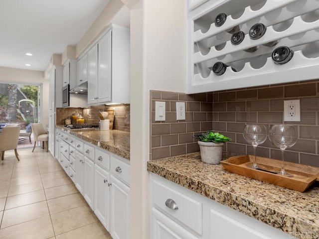 kitchen featuring light tile patterned floors, tasteful backsplash, light stone countertops, under cabinet range hood, and white cabinetry