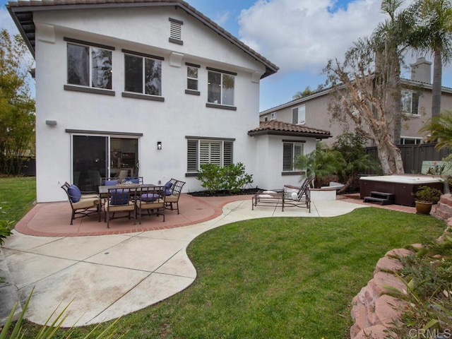 back of property with stucco siding, a hot tub, a lawn, and a patio