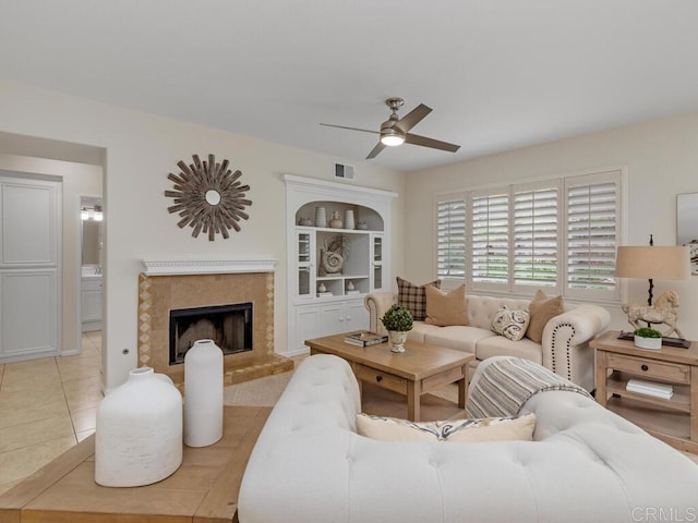 living area featuring light tile patterned floors, a fireplace, visible vents, and a ceiling fan