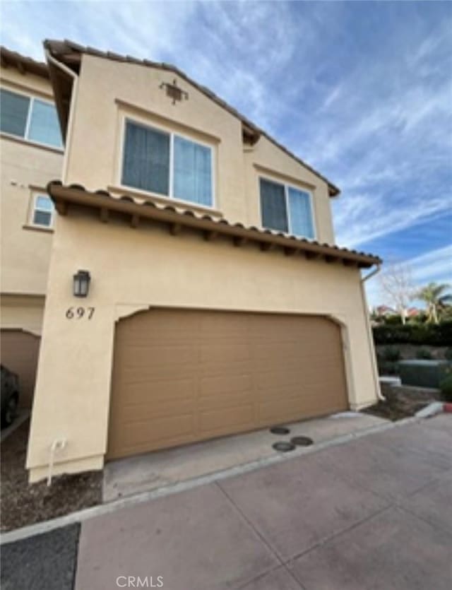 view of front facade featuring a tiled roof, an attached garage, and stucco siding