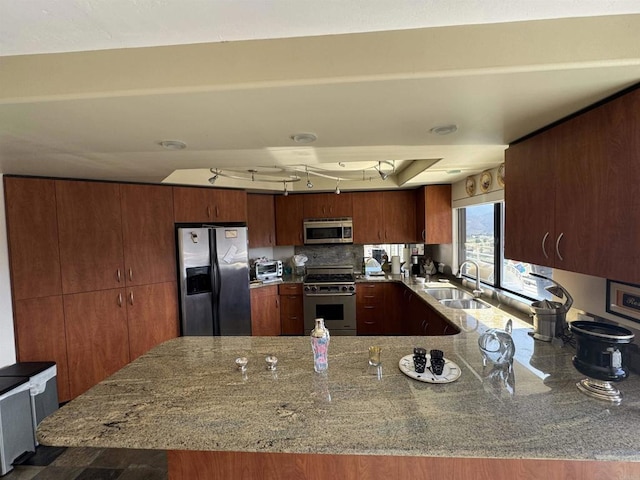kitchen featuring a peninsula, a sink, light stone counters, and appliances with stainless steel finishes