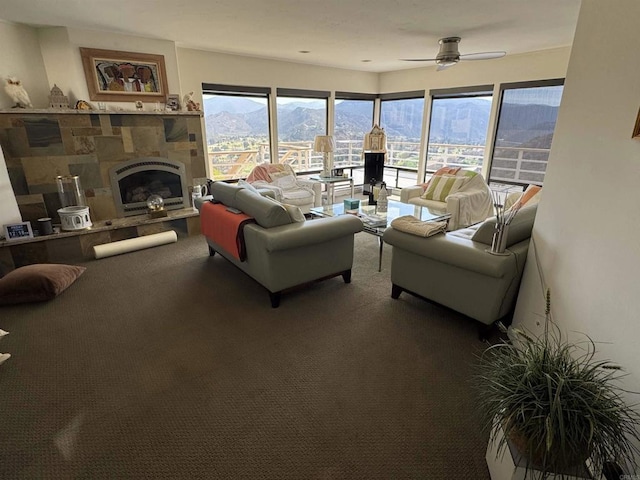 living room featuring a stone fireplace, a mountain view, ceiling fan, and carpet flooring