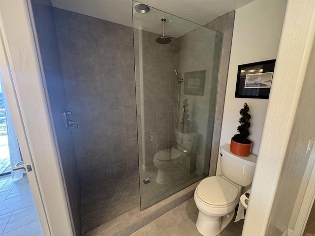 bathroom with tiled shower, toilet, and tile patterned flooring
