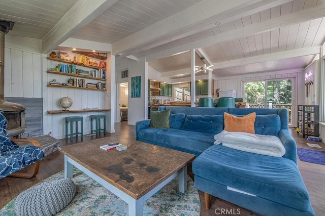 living room with a wood stove, a healthy amount of sunlight, vaulted ceiling with beams, and wood finished floors