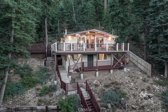 back of house with stairs, a deck, fence, and a view of trees