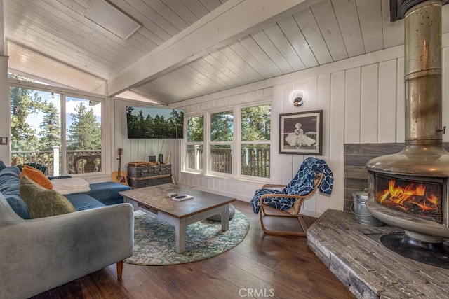 living area with lofted ceiling with beams, a wealth of natural light, wood finished floors, and a wood stove