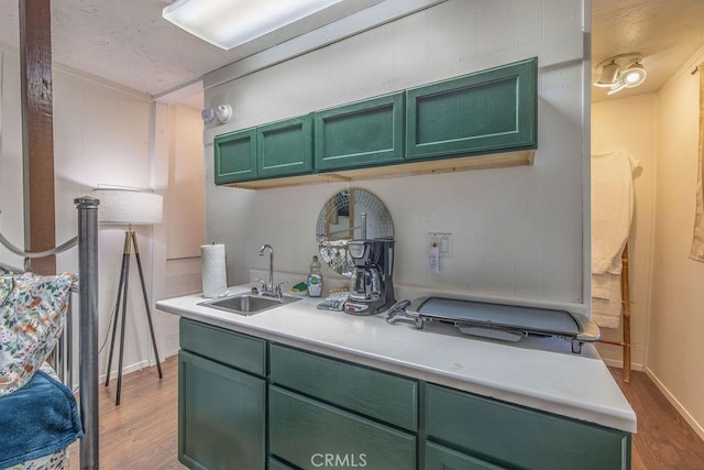 kitchen with a sink, light wood finished floors, light countertops, and green cabinetry