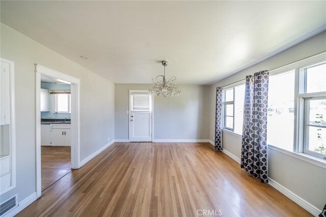 unfurnished dining area with a chandelier, wood finished floors, visible vents, and baseboards