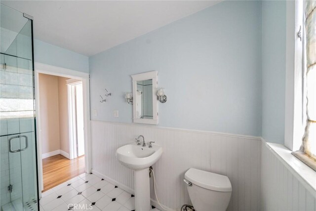 bathroom featuring a sink, wainscoting, a shower stall, and toilet