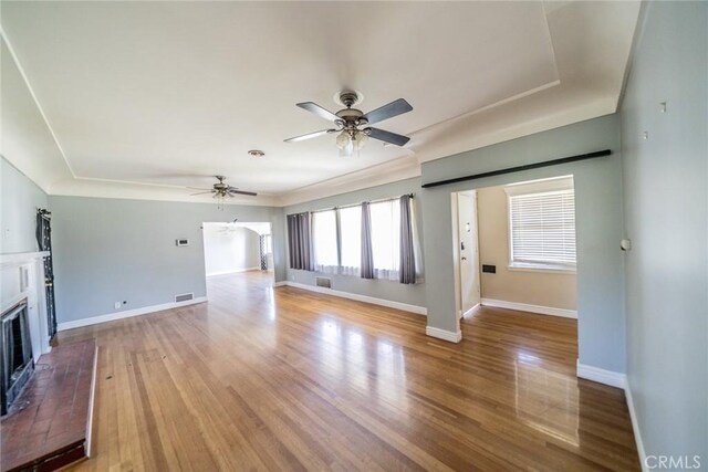 unfurnished living room with light wood finished floors, visible vents, baseboards, a fireplace with raised hearth, and a ceiling fan