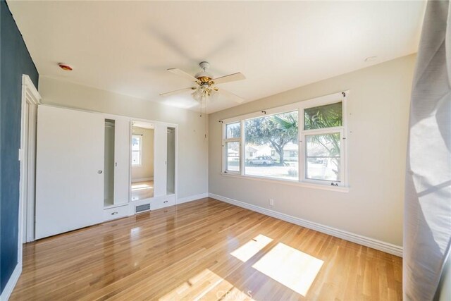 empty room featuring a ceiling fan, light wood-type flooring, visible vents, and baseboards