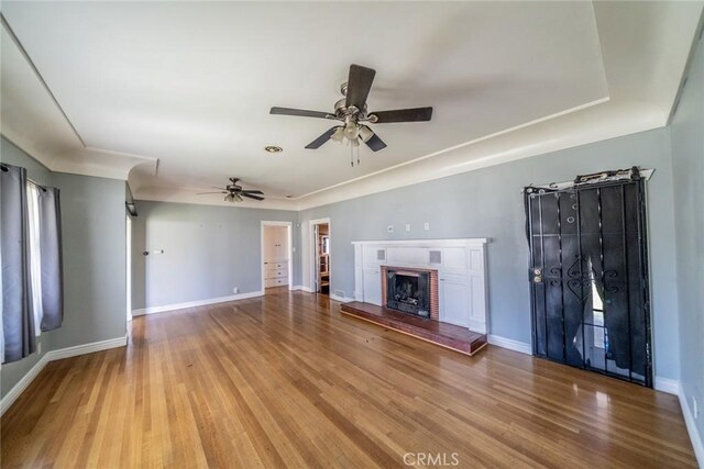 unfurnished living room featuring a brick fireplace, a ceiling fan, baseboards, and wood finished floors