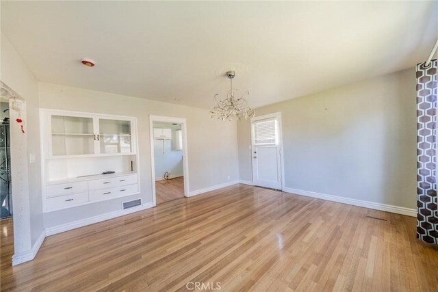 empty room featuring a chandelier, baseboards, visible vents, and light wood finished floors