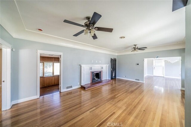 unfurnished living room featuring a fireplace with raised hearth, light wood finished floors, visible vents, and baseboards