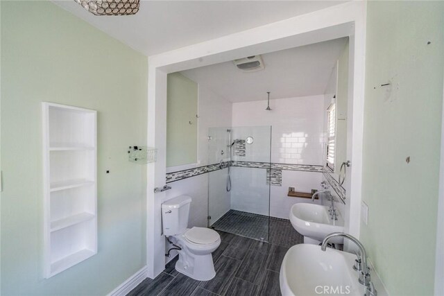 full bathroom with toilet, tile walls, a tile shower, and a sink