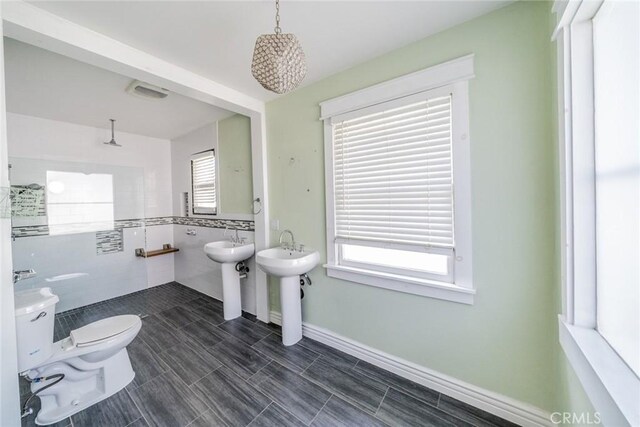 bathroom featuring toilet, a sink, walk in shower, and tile walls