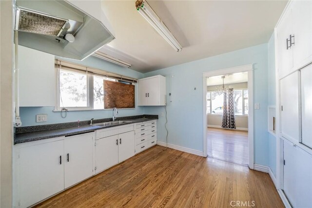 kitchen with baseboards, white cabinets, dark countertops, light wood-style flooring, and a sink