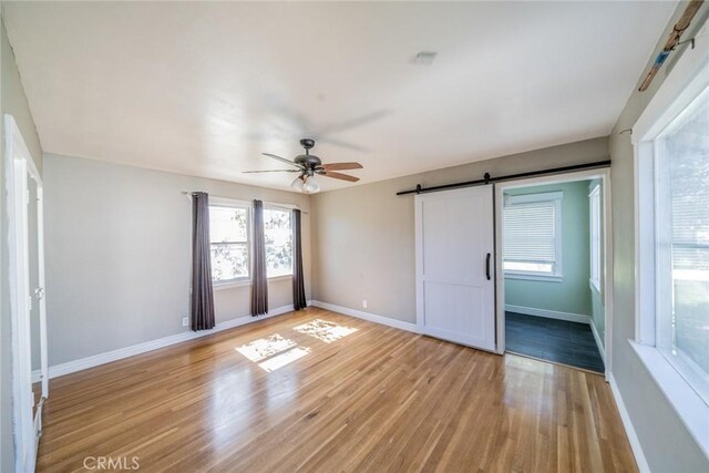 interior space featuring ceiling fan, a barn door, light wood-type flooring, and baseboards