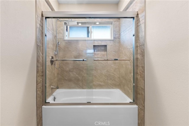 bathroom featuring combined bath / shower with glass door and a textured wall