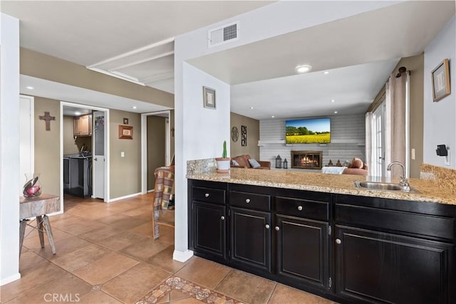 kitchen featuring visible vents, open floor plan, dark cabinetry, a brick fireplace, and a sink