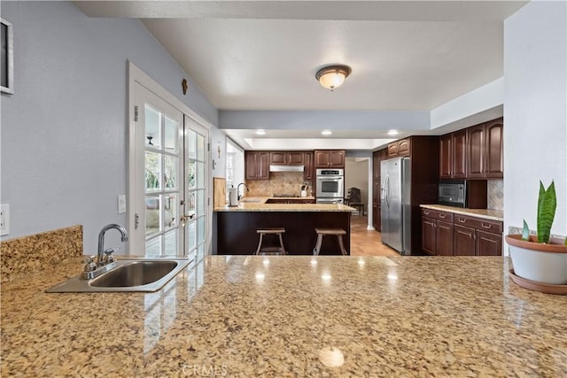 kitchen with tasteful backsplash, freestanding refrigerator, a peninsula, under cabinet range hood, and a sink