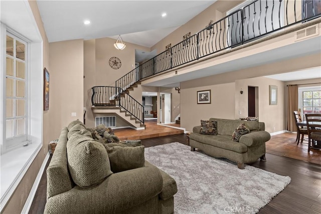 living area featuring a high ceiling, wood finished floors, visible vents, baseboards, and stairway