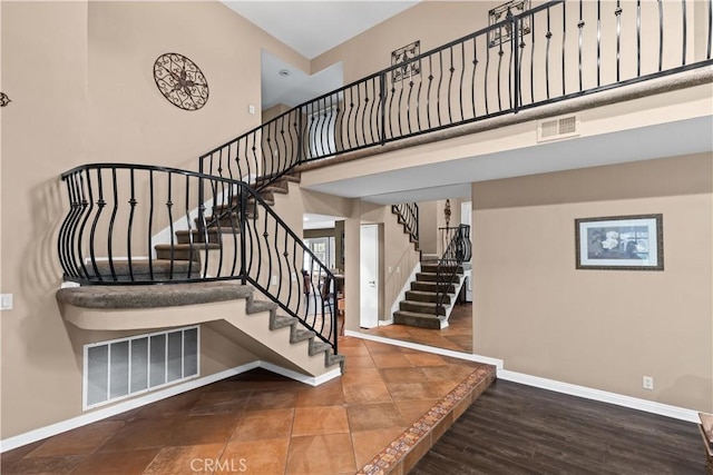 stairs featuring baseboards, visible vents, and a high ceiling