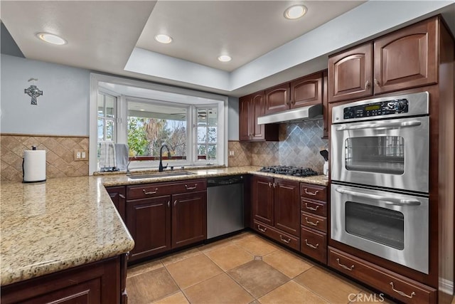 kitchen with stainless steel appliances, a sink, under cabinet range hood, and light stone counters