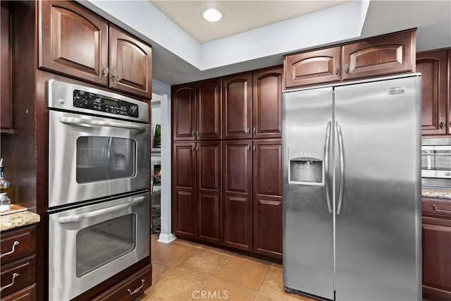 kitchen with light tile patterned floors, recessed lighting, appliances with stainless steel finishes, dark brown cabinetry, and light stone countertops