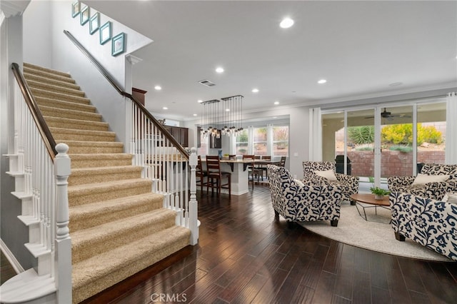 living area featuring dark wood-style floors, stairway, visible vents, and crown molding