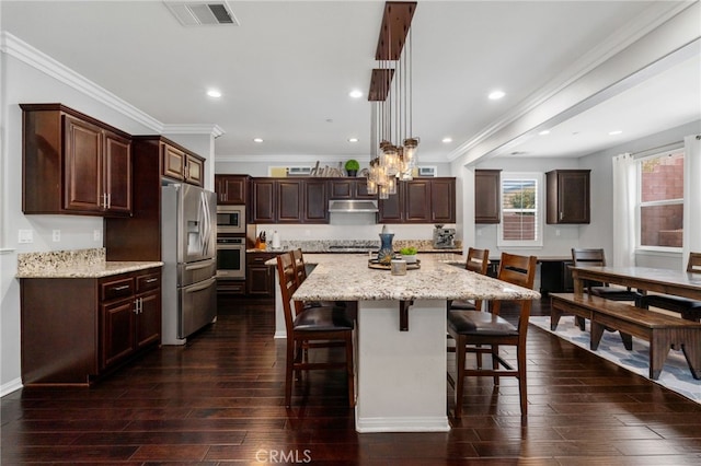 kitchen with dark wood finished floors, a breakfast bar area, stainless steel appliances, visible vents, and under cabinet range hood