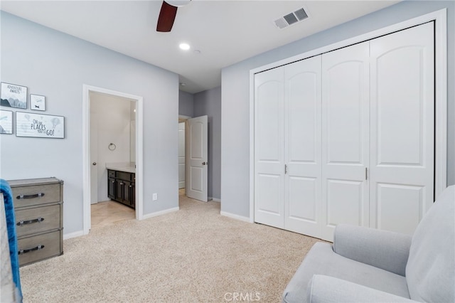 bedroom featuring a closet, light colored carpet, visible vents, ensuite bathroom, and baseboards