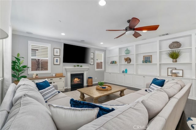 living area featuring crown molding, recessed lighting, visible vents, a glass covered fireplace, and wood finished floors