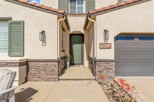 property entrance with a garage, stone siding, a tiled roof, and stucco siding