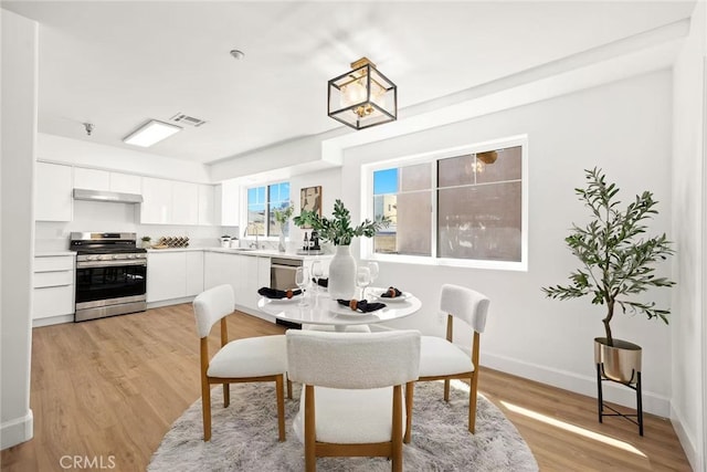 dining area with baseboards, visible vents, and light wood finished floors