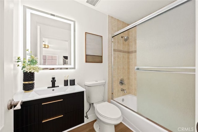 bathroom with toilet, wood finished floors, vanity, visible vents, and combined bath / shower with glass door