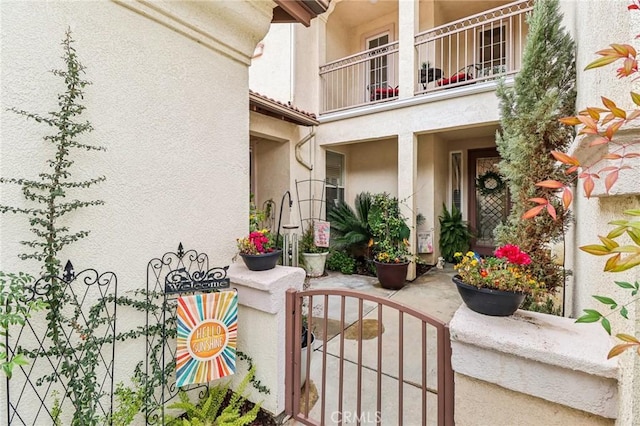 exterior space with a balcony, a gate, fence, and stucco siding