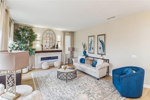 living area featuring a glass covered fireplace, baseboards, visible vents, and wood finished floors