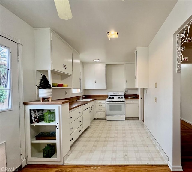 kitchen with a sink, dark countertops, white cabinetry, light floors, and white gas range