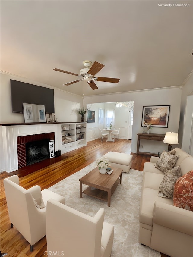 living room with a fireplace, crown molding, wood finished floors, and ceiling fan