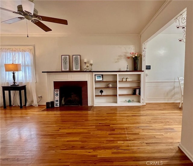 unfurnished living room with ceiling fan, wood finished floors, ornamental molding, and a fireplace