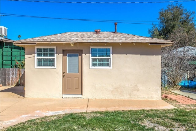 bungalow with stucco siding, roof with shingles, and fence