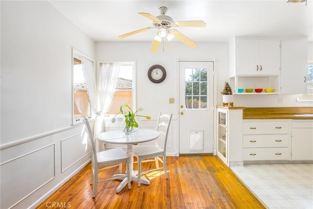 dining area with wainscoting, a decorative wall, light wood-style flooring, and ceiling fan