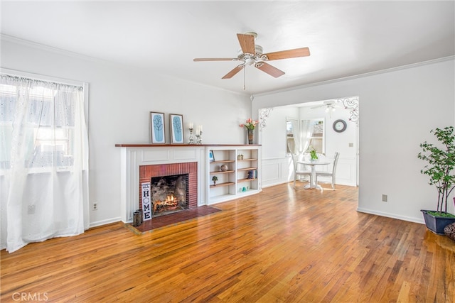 unfurnished living room with ceiling fan, a brick fireplace, hardwood / wood-style floors, and ornamental molding