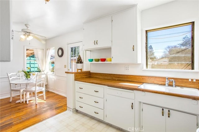 kitchen with a sink, open shelves, white cabinets, a decorative wall, and light floors