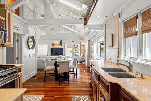 kitchen featuring a sink, appliances with stainless steel finishes, dark wood-style flooring, open floor plan, and vaulted ceiling with beams