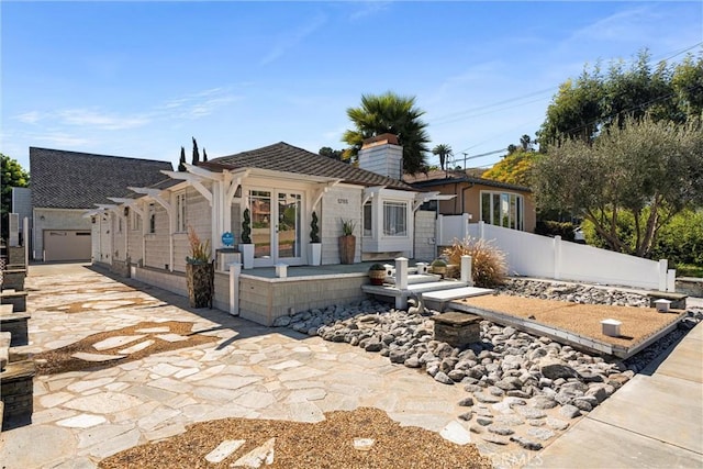 rear view of property with a chimney, fence, a garage, driveway, and french doors