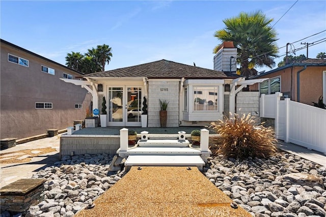 view of front of home with french doors, fence, roof with shingles, and a chimney