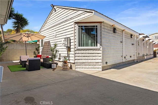 view of property exterior with an outdoor hangout area, fence, and a patio area